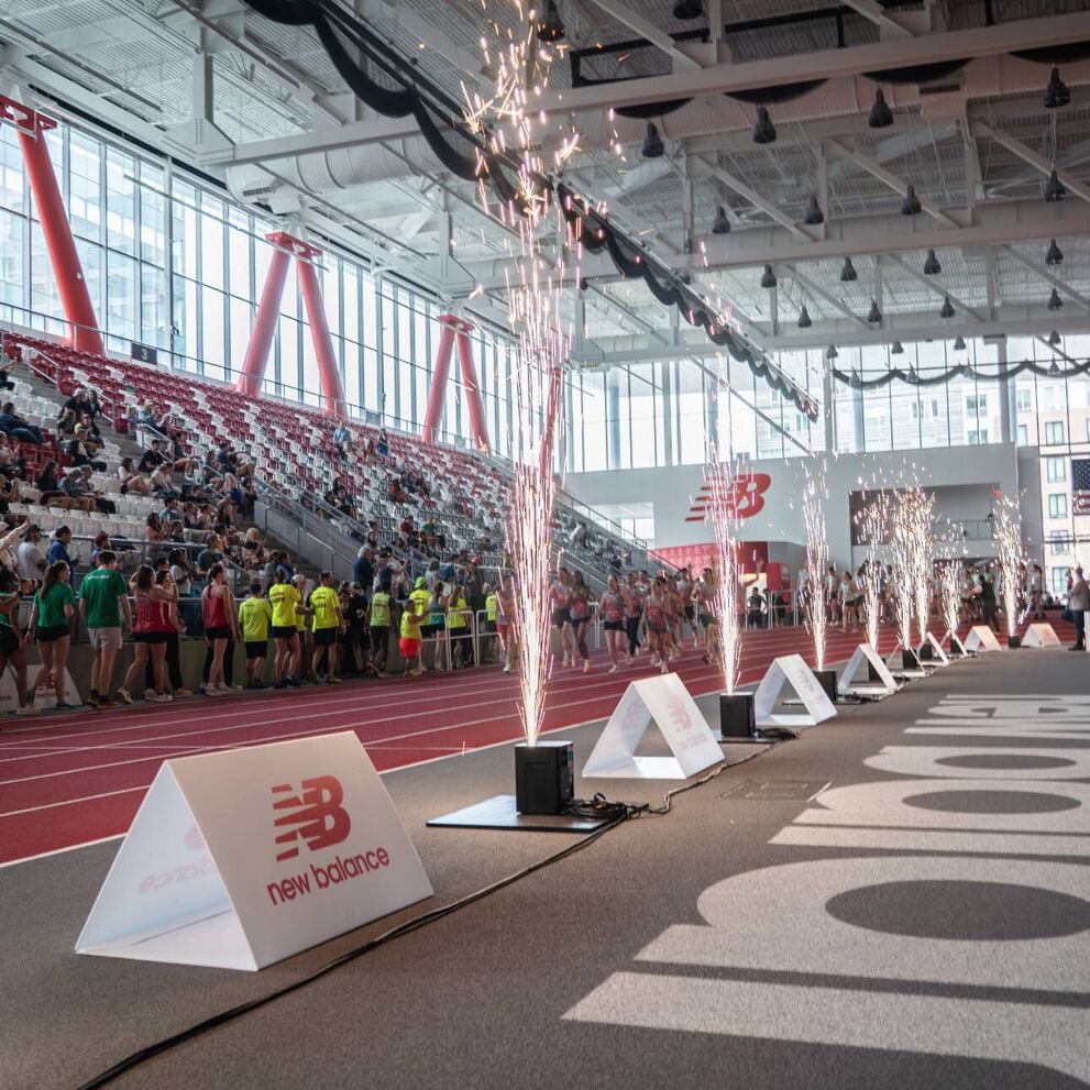 A New Balance track event with people in the stands and sparklers spraying into the air.
